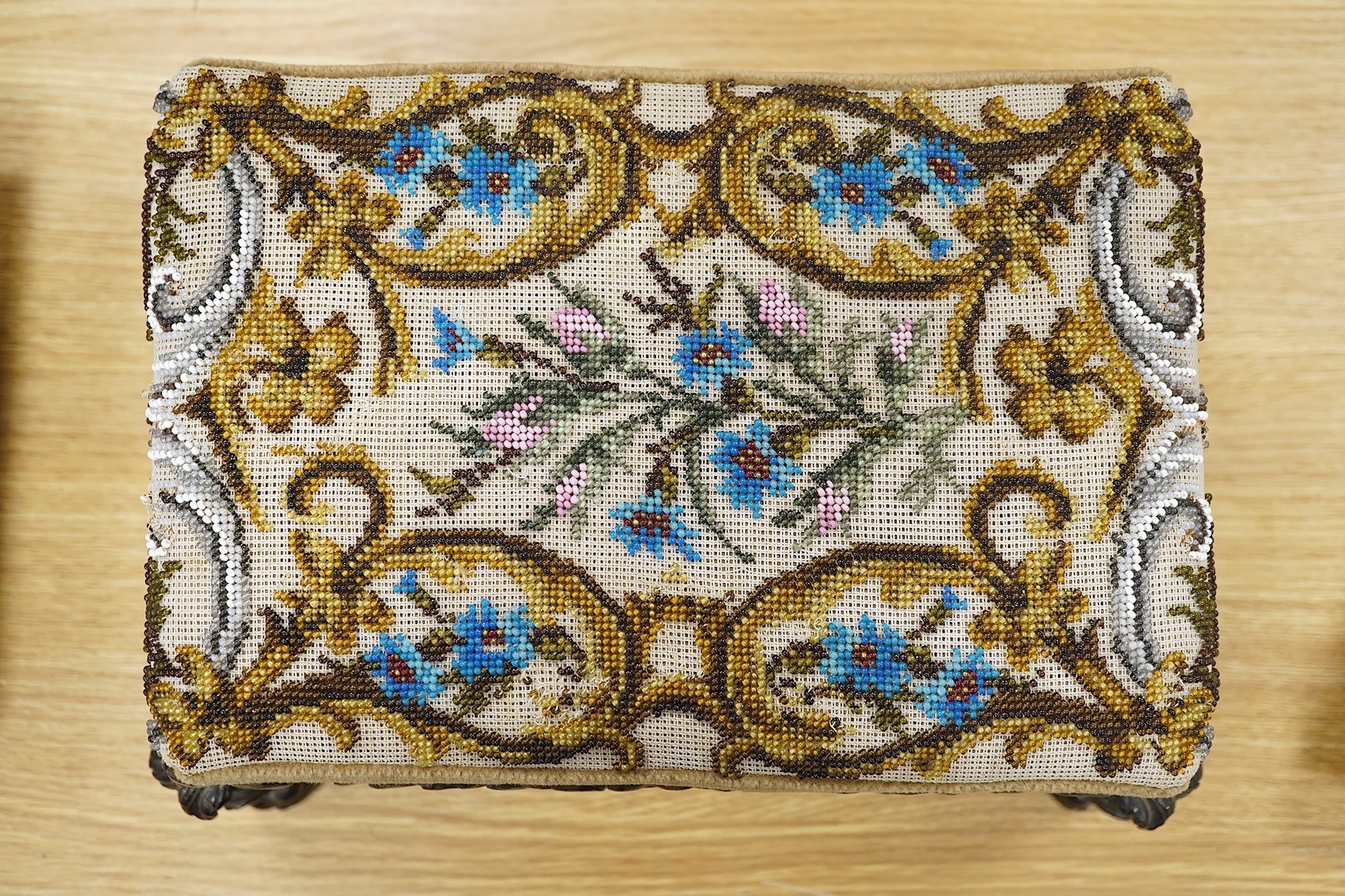 A 19th century ornately carved paw foot, Berlin beadwork upholstered footstool, the bead work a scrolling multi-coloured floral pattern, upholstered into a heavily carved frame and legs on carved paw feet, beadwork 21cm